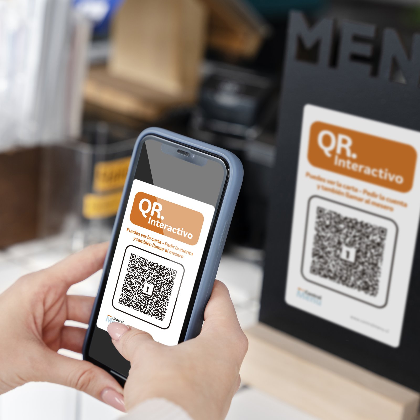 Una mano sostiene un celular que escanea el código QR interactivo de Control Menú, junto a un atril de mesa con el mismo QR