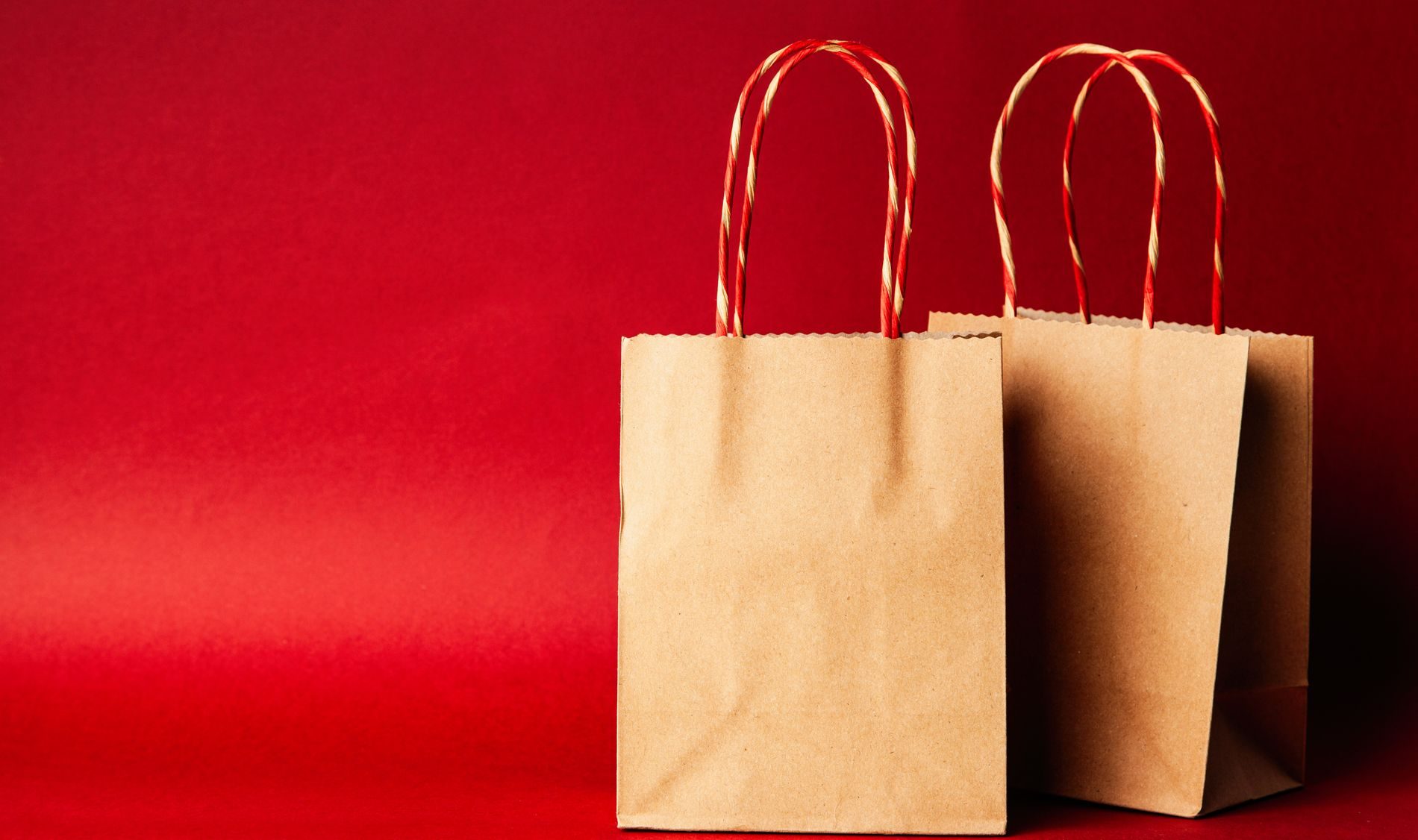 Dos bolsas de papel kraft con manillas de cordel sobre un fondo rojo
