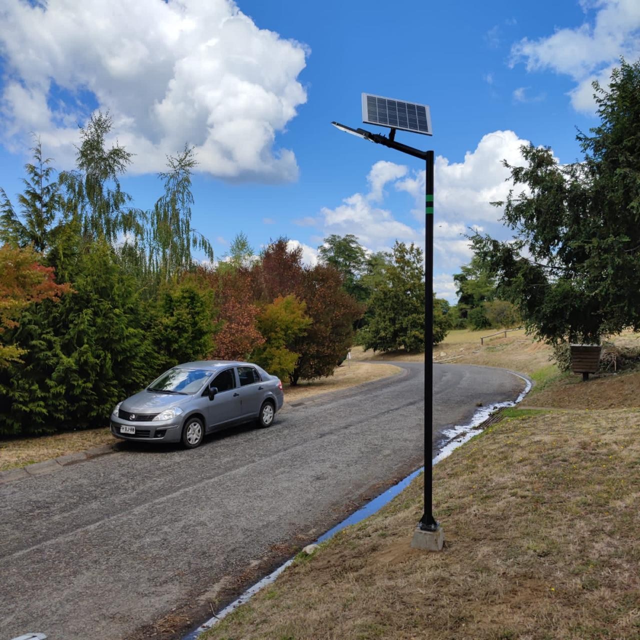 Luminaria solar en poste de acero junto a un camino, de día