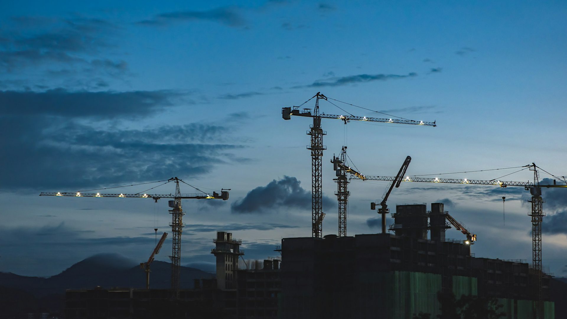 Grúas torre iluminadas sobre una obra en construcción al anochecer