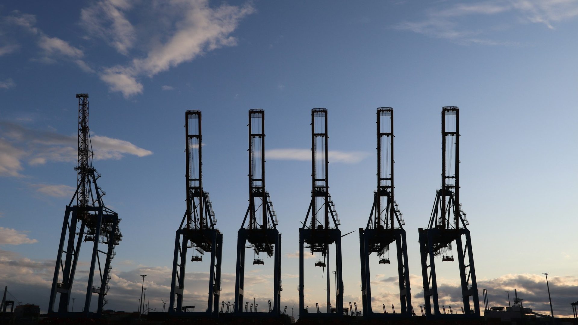 Grúas de un puerto de carga a contraluz bajo un cielo azul