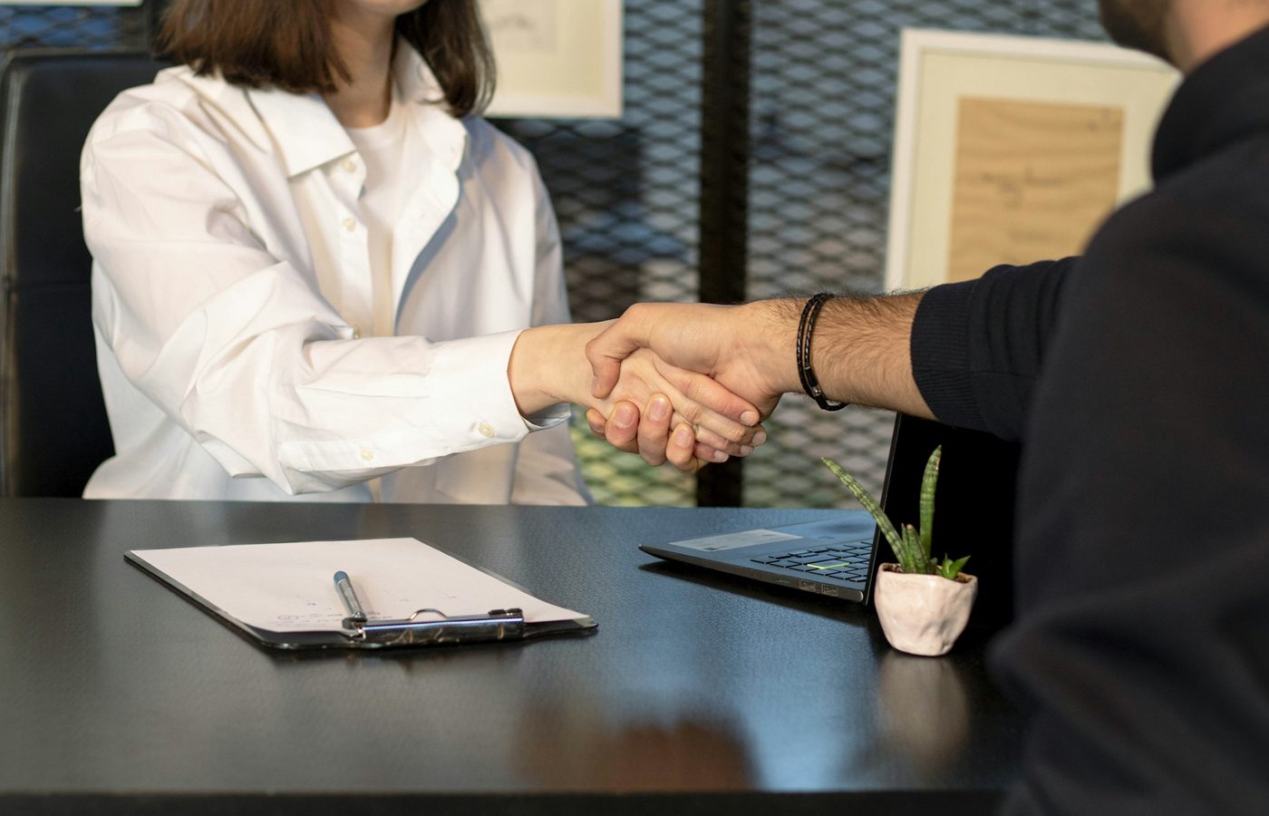 Dos personas se dan la mano sobre un escritorio con documentos