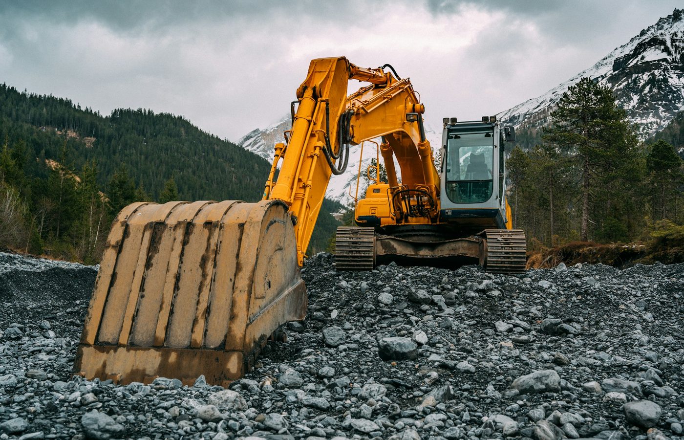 Excavadora amarilla sobre un terreno de grava con montañas al fondo